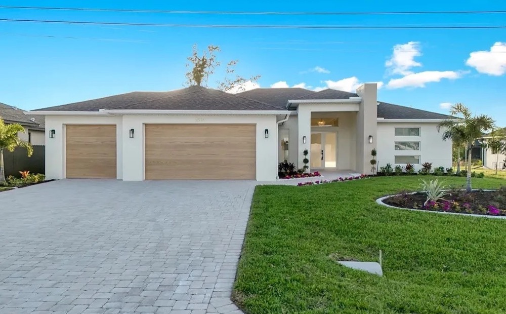 White single-story home with a three-car garage, a paver driveway and a landscaped front yard under a blue sky