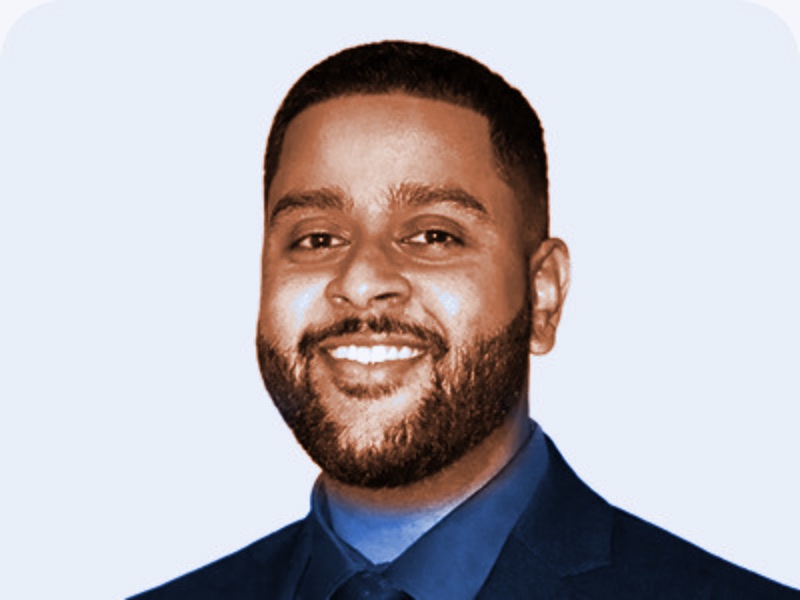 Portrait of Travis Ramballie, smiling, with a short beard, in a dark jacket