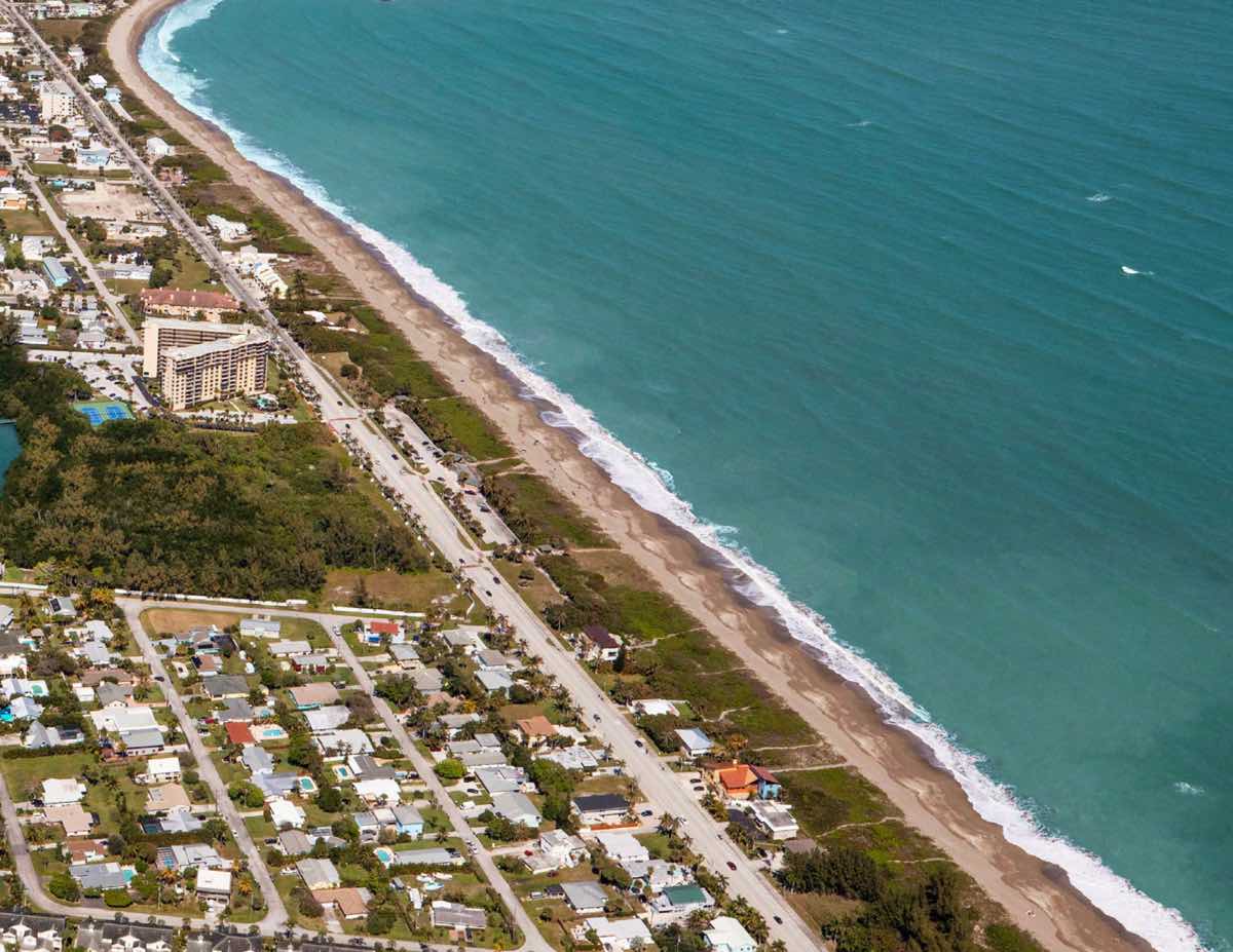 Aerial photograph of the Atlantic coastline with a beach road and low-rise neighborhood along the shore